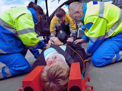 Paramedics and a fireman strapping a wounded woman with a neck brace on a stretcher.