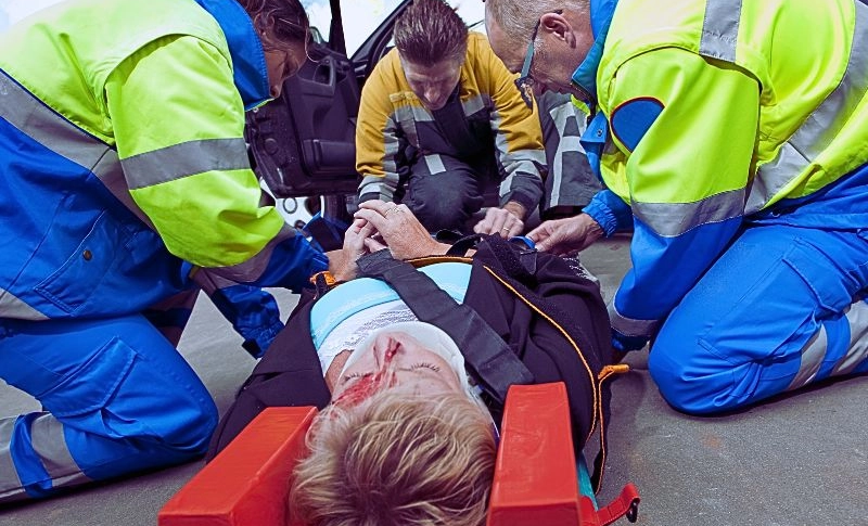 Paramedics and a fireman strapping a wounded woman with a neck brace on a stretcher.