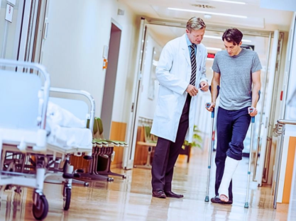 Man with broken leg talking with doctor in hospital corridor.