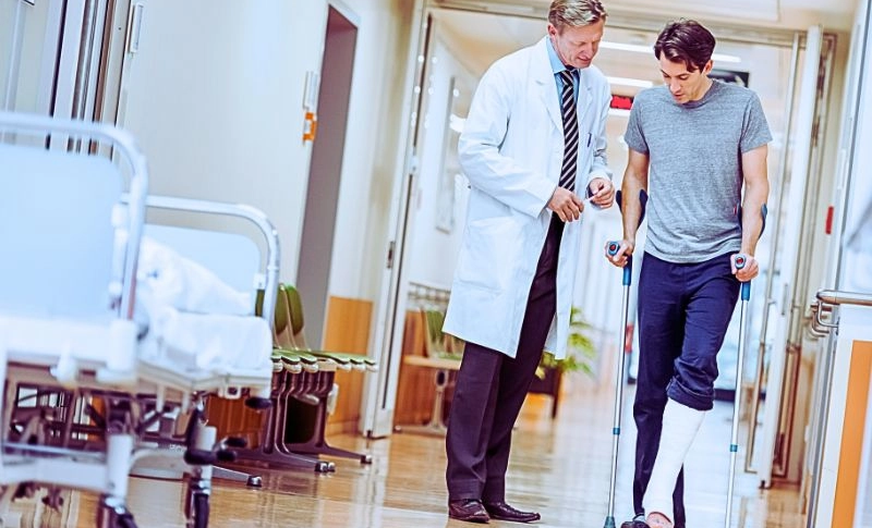 Man with broken leg talking with doctor in hospital corridor.