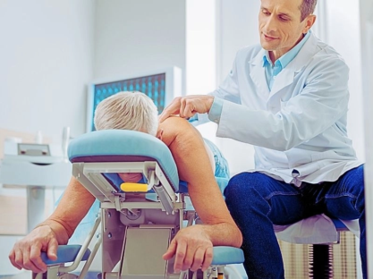 Male doctor sitting near his patient and massaging his spine.