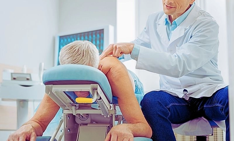 Male doctor sitting near his patient and massaging his spine.