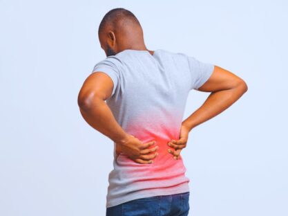 Guy holding both hands on lower back, pain in spine, inflamed zone highlighted in red.