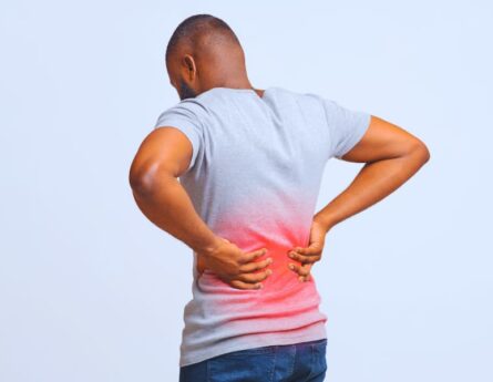 Guy holding both hands on lower back, pain in spine, inflamed zone highlighted in red.