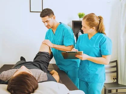 Young physiotherapist examining customer's leg while colleague noting in clipboard at the hospital.