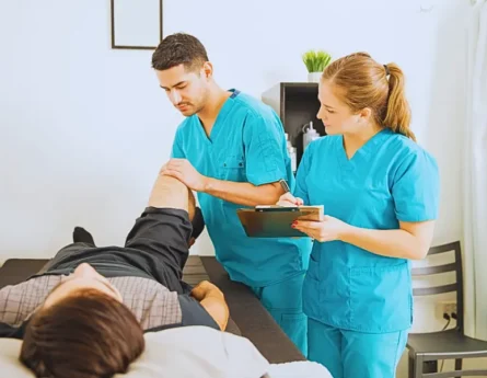 Young physiotherapist examining customer's leg while colleague noting in clipboard at the hospital.