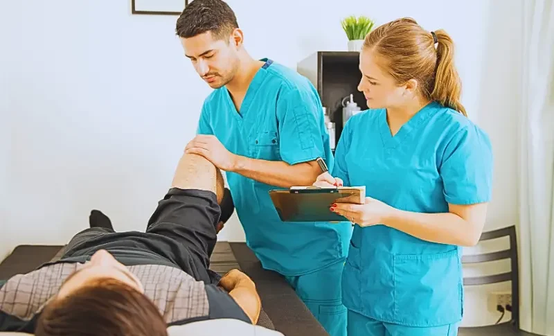 Young physiotherapist examining customer's leg while colleague noting in clipboard at the hospital.