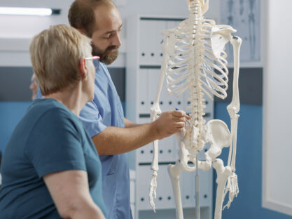 24689489 male doctor pointing human skeleton show spinal cord explain mechanical disorders rehabilitation cabinet specialist explaining back bones system physical therapy