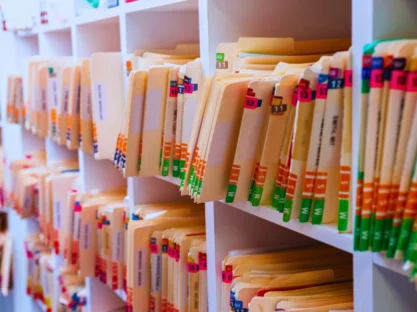 Shelves filled with organized medical records in folders. Each folder has colored tabs and labels, likely for easy identification and categorization.